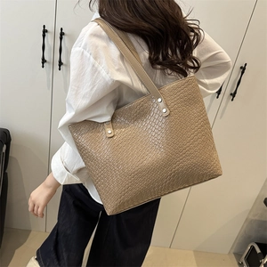 Detail of grey crocodile embossed tote bag worn on shoulder in a minimalist indoor setting