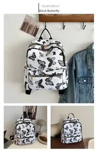 Detailed view of white nylon backpack featuring black butterfly prints and metal zippers