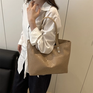 Close-up of khaki woven leather tote bag featuring durable silver rivets and shoulder strap