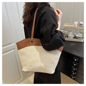 Detail of woven straw tote bag with brown leather straps and metal ring connector