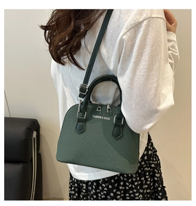 Detail of dark green shell bag with woven texture worn over shoulder by a model