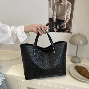 Close-up of black woven leather tote bag with silver rivets and textured pattern