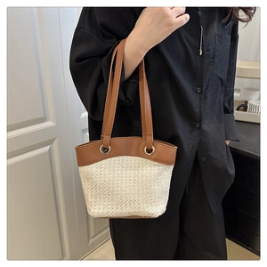 Detail of woven straw tote bag featuring brown leather trim and metal eyelet accents