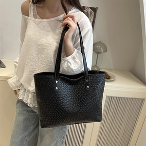 Detail shot of the black woven leather texture and silver rivets on the tote bag