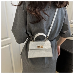 Detailed view of silver glitter mini Kelly bag with gold metal lock and shoulder strap