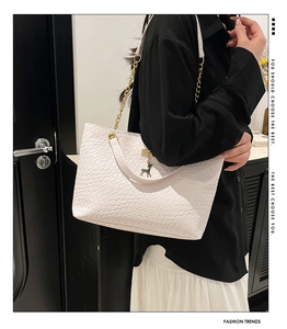 Close-up of white woven leather tote bag with gold chain strap and deer charm detail