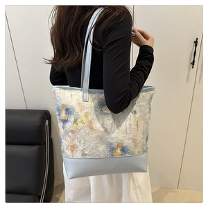 Detail of floral texture on tote bag with light blue leather straps shown on shoulder