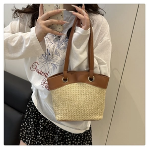 Detail of handwoven straw tote bag with brown faux leather trim and slender handles