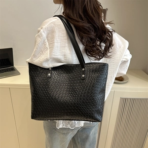 Detail of black woven leather tote bag with checkerboard pattern and metal rivets