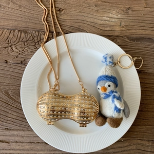 Mini peanut shaped evening bag with crystals and a gold chain on a wooden table