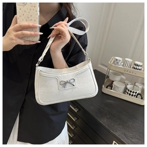 Detail of white crocodile pattern embossed leather handbag with metal bow accessory