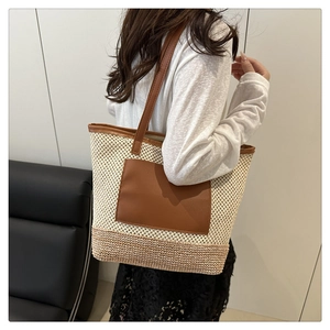 Detail view of woven straw tote bag with brown leather pocket and long shoulder straps