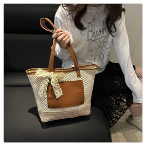 Detail of woven straw tote bag with brown leather trim and white lace bow detail