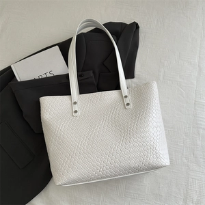 Macro view of white textured tote bag featuring woven crocodile pattern and silver rivets