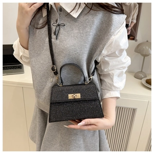 Detail of glittery black mini Kelly bag featuring a gold metal clasp and a top handle