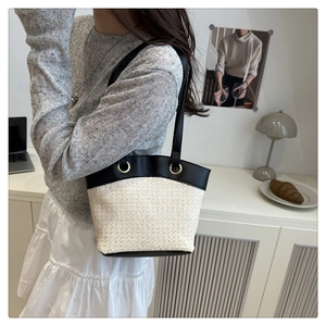Detail of large woven straw tote bag with black leather patchwork and gold metal eyelets