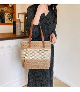Primer plano del bolso tote de paja a rayas con asa de cuero y detalle de borla decorativa