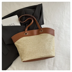 Close-up of beige woven straw tote bag with brown leather handles and metallic ring detail