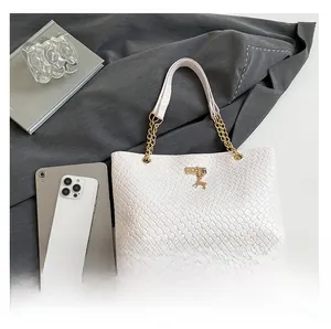 Detail of white woven tote bag featuring gold deer charm and chain shoulder strap