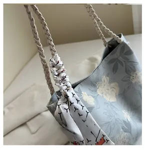 Detail of floral tote bag featuring woven strap and decorative geometric silk scarf accent