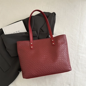 Detail of red woven leather tote bag featuring classic intrecciato texture and rivets