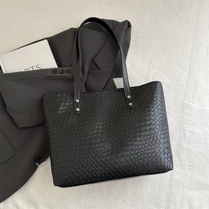 Detailed close-up of woven leather texture and silver rivets on a black tote bag