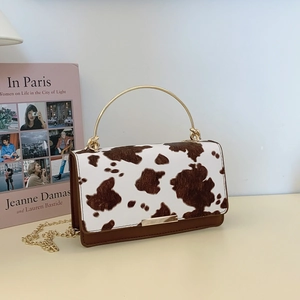 Sac bandoulière imprimé vache avec poignée dorée et chaîne sur un bureau chic