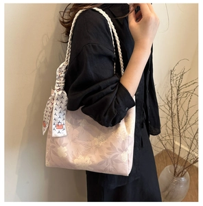Detail of pink floral tote bag with white woven handles and decorative scarf on a model