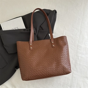 Detail of a brown woven leather tote bag with sturdy straps and metallic rivets