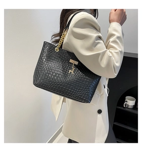 Detail of black woven tote bag featuring gold chain strap and deer charm on a model