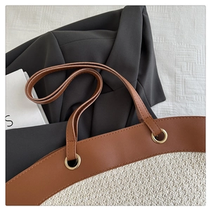 Detailed close-up of woven tote bag with brown leather trim and golden hardware