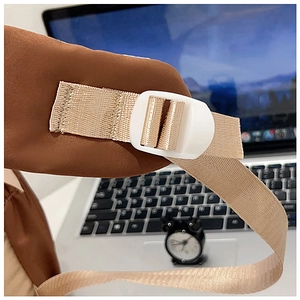 Close-up of adjustable beige strap and white plastic buckle on a brown canvas backpack