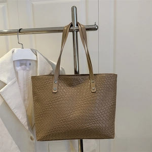 Detail of tan woven leather tote bag with sturdy shoulder straps and silver rivets