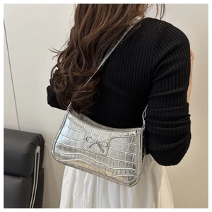Silver crocodile pattern underarm bag with metal bow detail worn over the shoulder