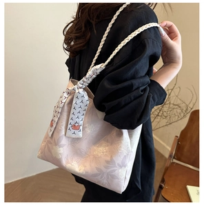 Detail of light pink floral tote bag featuring woven straps and elegant silk scarf accent