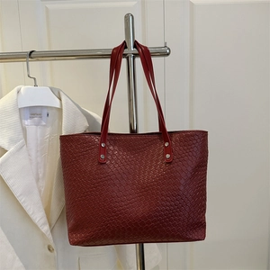 Close-up of wine red woven leather tote bag featuring detailed texture and silver rivets