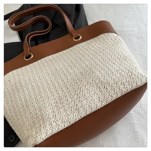 Detail of woven straw tote bag featuring brown leather trim and metallic buckle accents