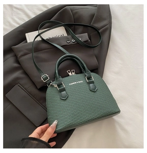 Detail of dark green shell bag with woven texture, dual handles and fashion logo
