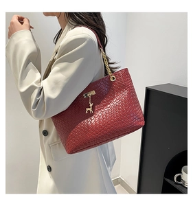 Detail of burgundy woven tote bag with gold deer charm and chain shoulder strap