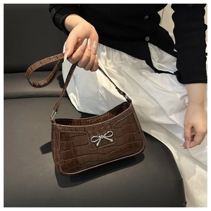 Detail of dark brown faux crocodile leather shoulder bag with a silver bow ornament