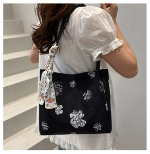 Detail of black tote bag with white floral print and a decorative silk scarf on the strap