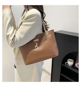 Close-up of brown woven tote bag with gold chain strap and deer charm accessory