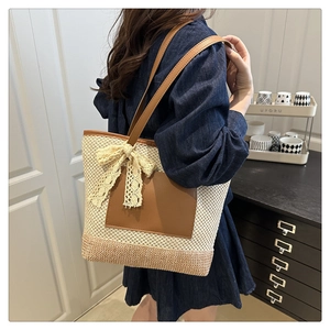 Detail of handwoven straw tote bag with brown leather straps and beige lace bow