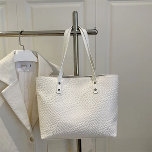 Close-up of the white woven texture tote bag featuring silver rivet hardware detail