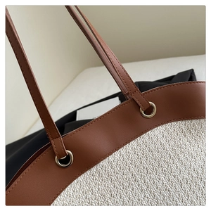 Detail of the leather trim and metal ring hardware on the woven straw tote bag