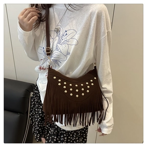 Macro shot of brown suede crossbody bag with vintage gold rivets and long fringe tassels