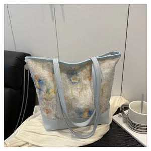 Detail of light blue floral lace tote bag with leather trim on a stylish couch