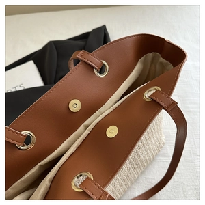 Detail of magnetic closure and faux leather trim on a large woven straw tote bag