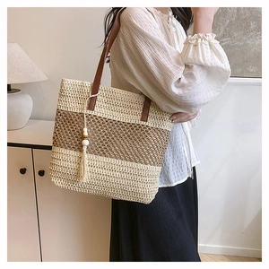 Detail of straw tote bag featuring contrast stripes, leather straps and beaded tassels
