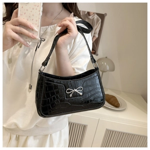 Detailed close-up of glossy crocodile texture and silver bow buckle on black handbag